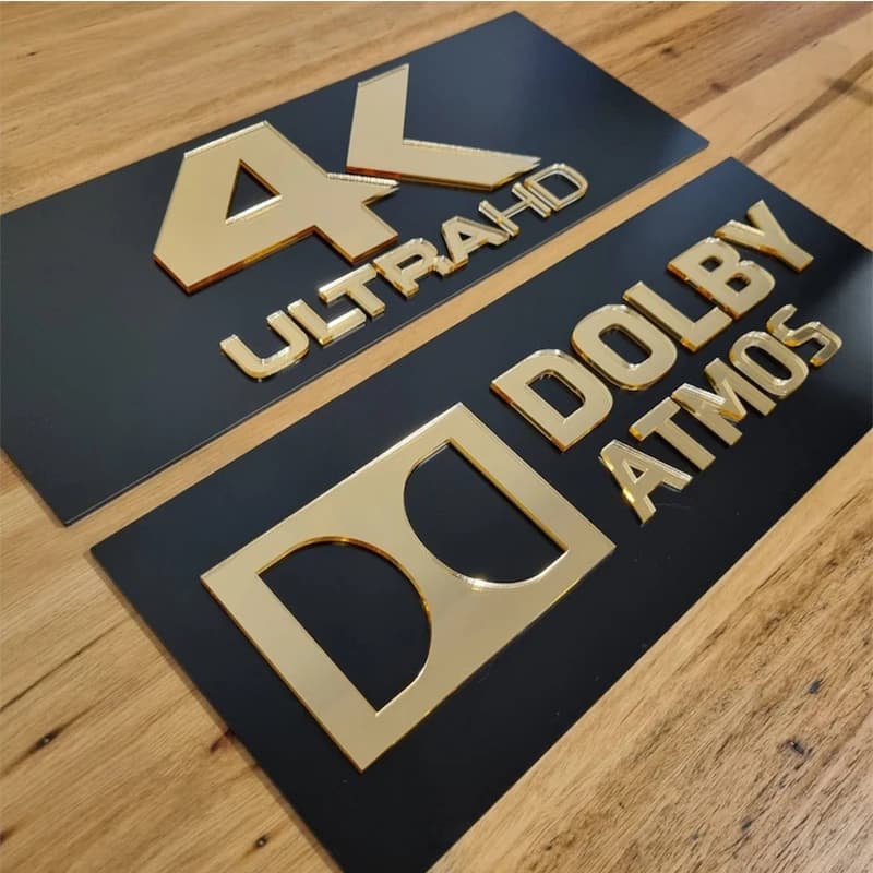 Heimkino 3D Wandschilder in Gold-Acryl — 4K Ultra HD und Dolby Atmos nebeneinander auf Holzoberfläche